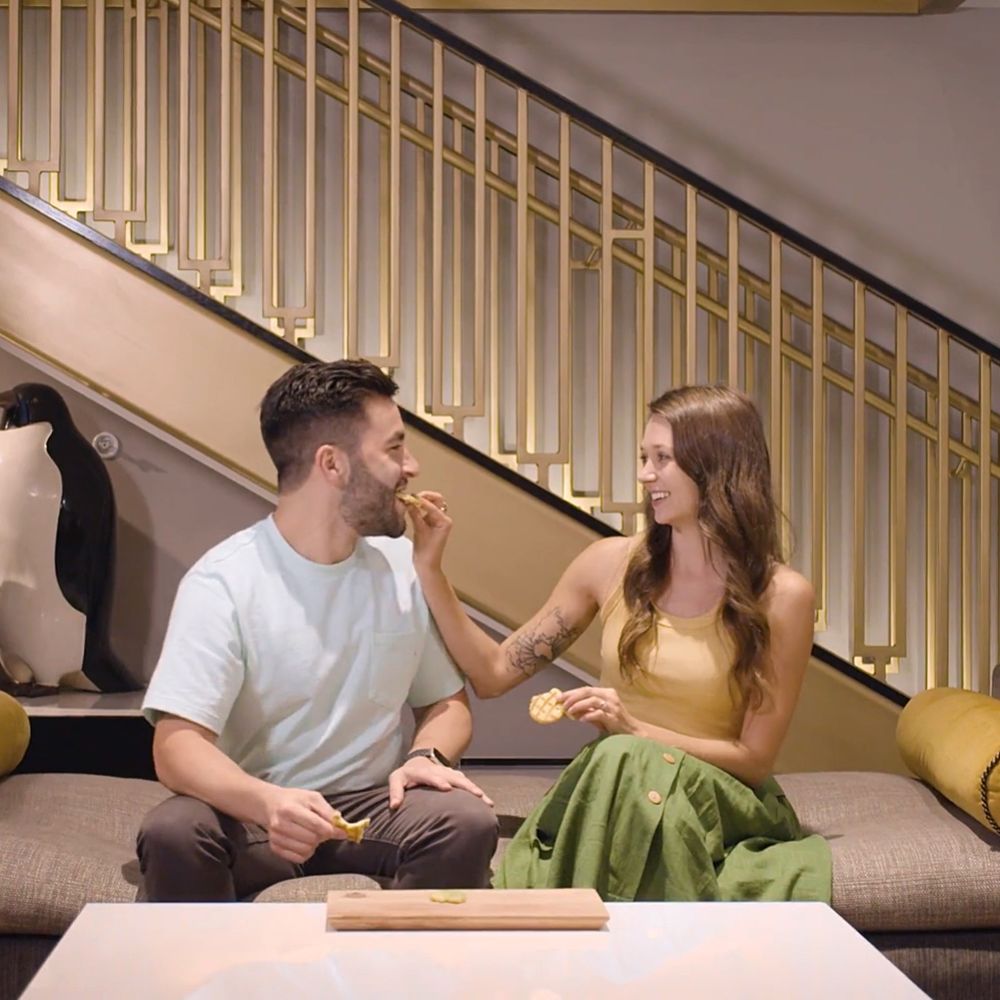 A Man And Woman Sitting On A Couch Eating
